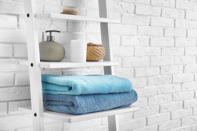Photo of Clean soft towels and soap dispenser on shelves near white brick wall