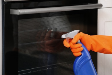 Photo of Woman cleaning oven with detergent in kitchen, closeup