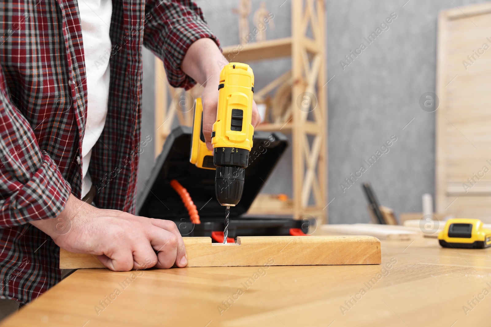 Photo of Young handyman working with electric drill at table in workshop, closeup