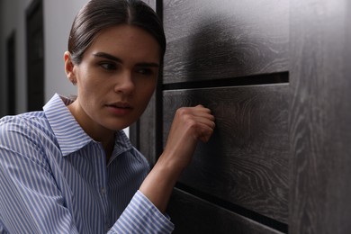 Woman in shirt knocking on door indoors