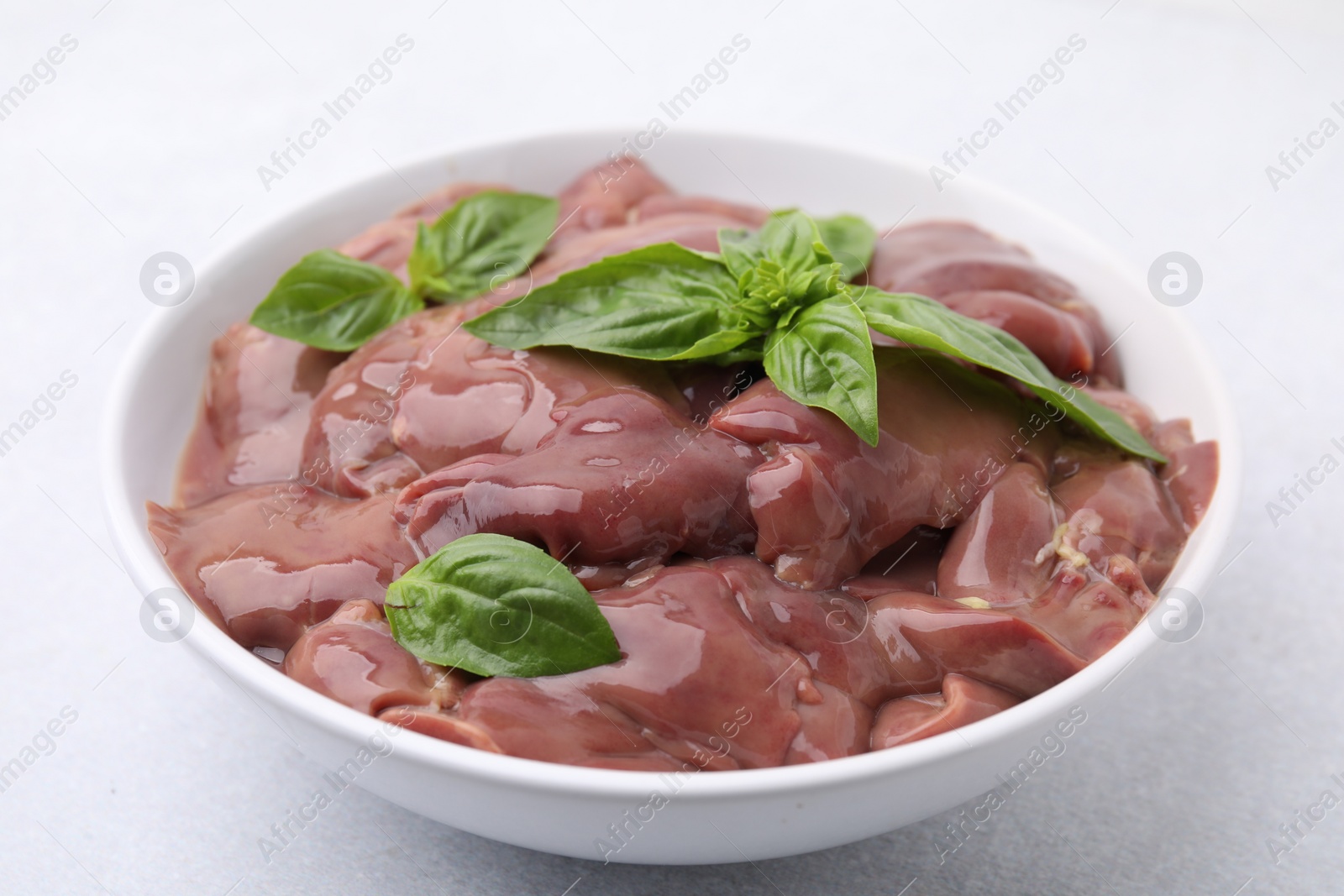 Photo of Bowl with raw chicken liver and basil on white table, closeup