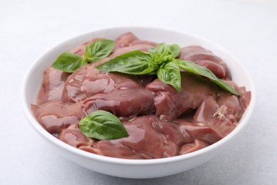 Bowl with raw chicken liver and basil on white table, closeup