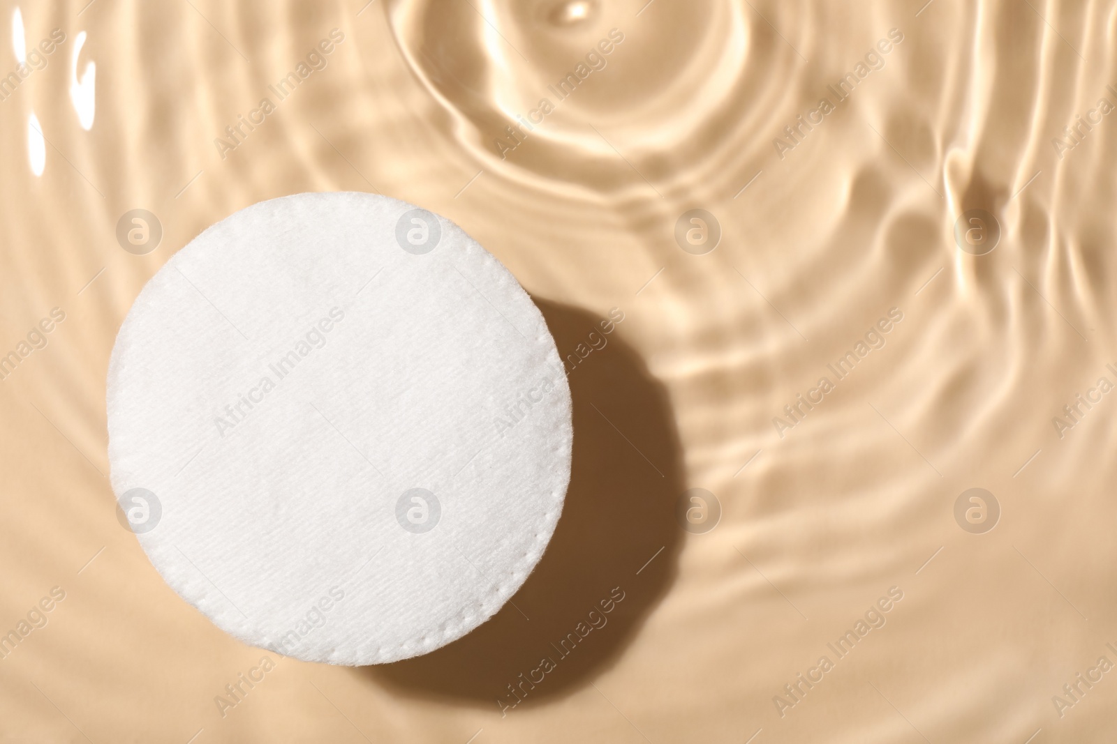 Photo of Cotton pad and micellar water on beige background, top view. Space for text