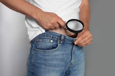 Photo of Man examining intimate area with magnifying glass on grey background, closeup. Genital herpes