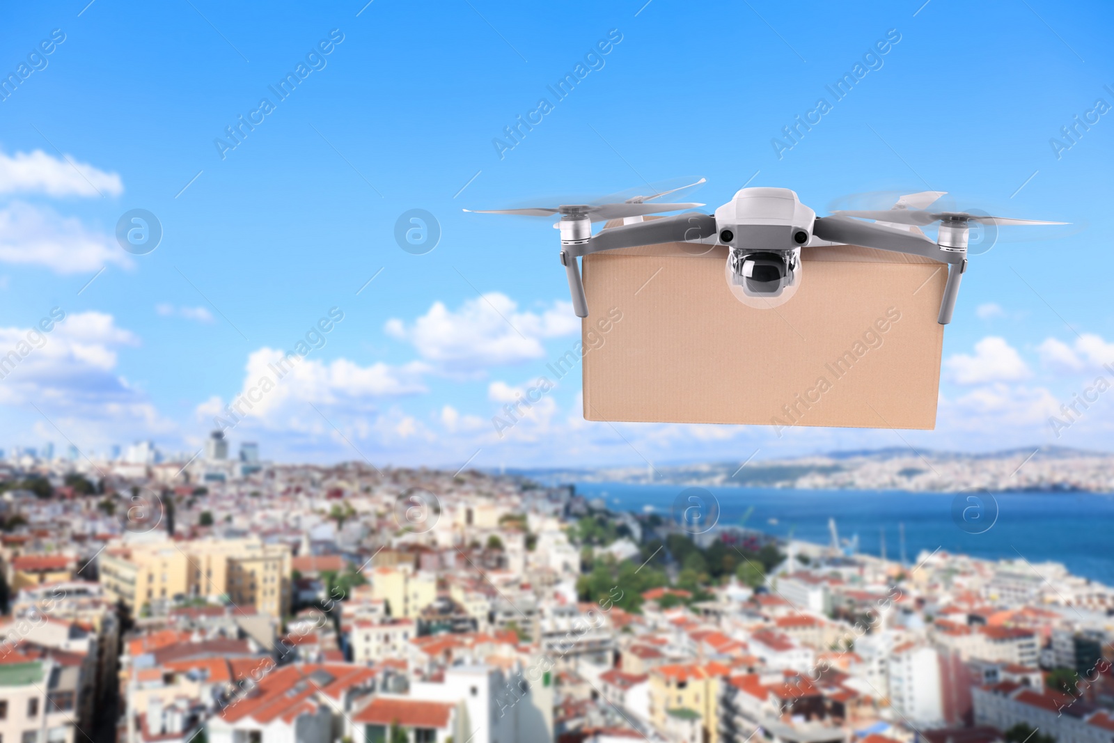 Image of Modern drone with carton box flying above city on sunny day. Delivery service 