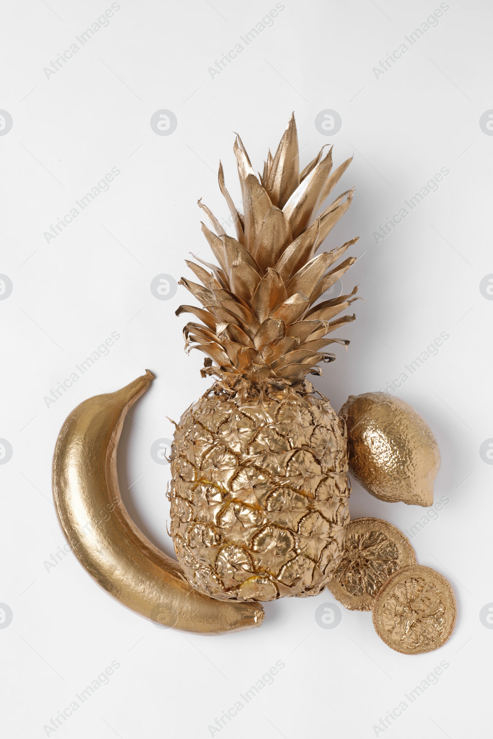 Photo of Shiny golden pineapple, banana, lemon and dry orange slices on white background, flat lay. Decor elements