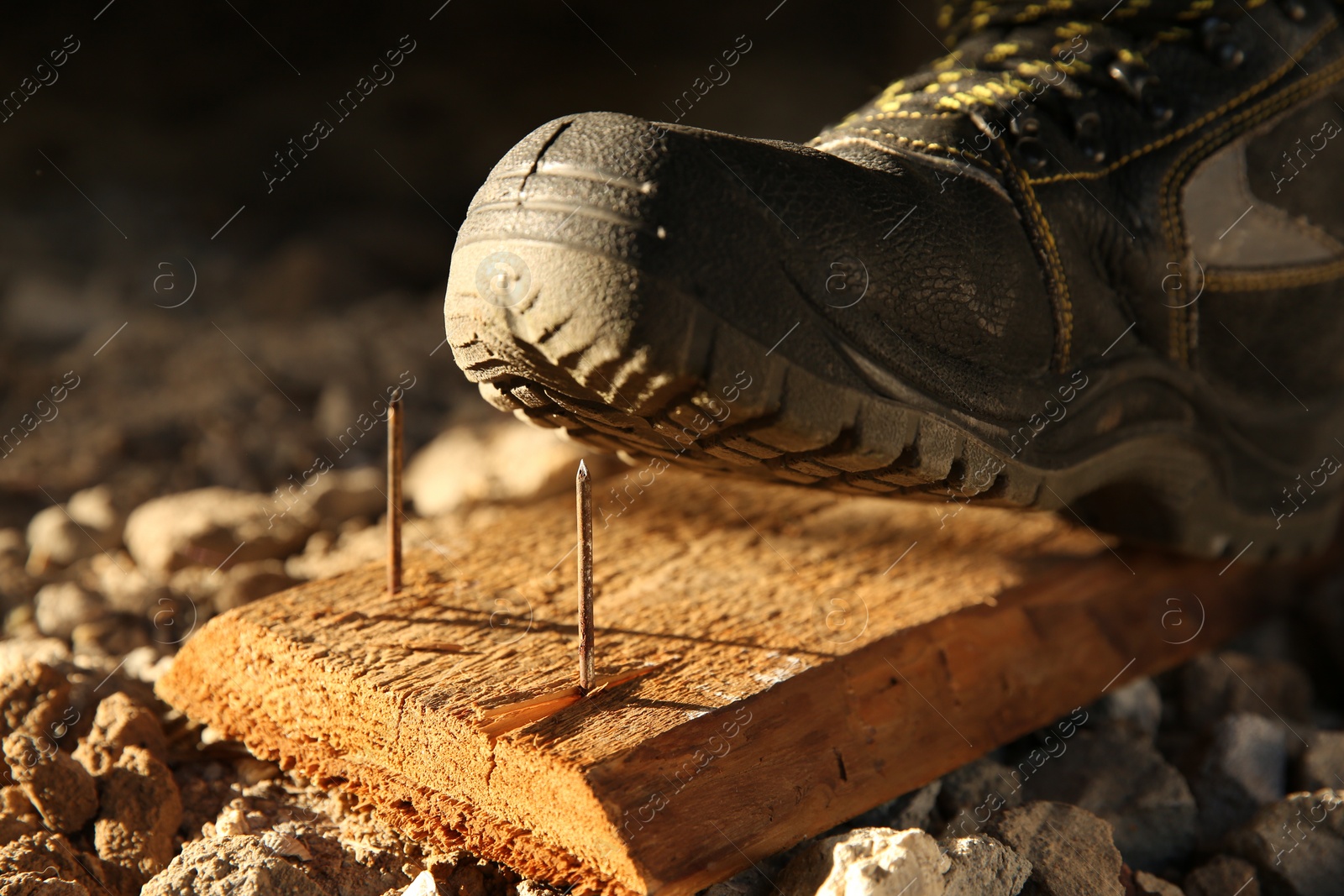 Photo of Careless worker stepping on nails in wooden plank, closeup