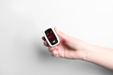 Photo of Woman holding fingertip pulse oximeter on white background, closeup