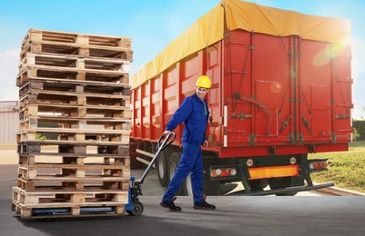 Image of Worker moving wooden pallets with manual forklift and modern truck outdoors