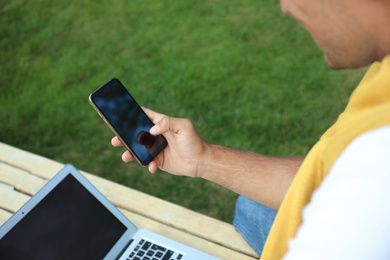 Man with smartphone and laptop in park, closeup