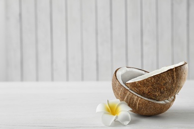 Photo of Halves of coconut and flower on white wooden table. Space for text