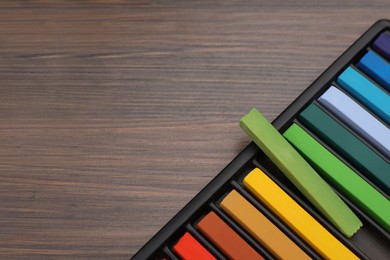 Photo of Colorful pastels in tray on wooden table, top view with space for text. Drawing materials