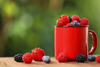 Photo of Mug with different fresh ripe berries on wooden table outdoors. Space for text
