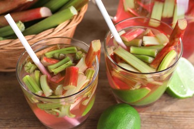 Glasses of tasty rhubarb cocktail with lime fruits on wooden table, closeup