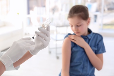 Doctor filling syringe with medicine and child on background. Vaccination day