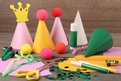 Photo of Different stationery and materials for creation of colorful party hats on wooden table. Handmade decorations