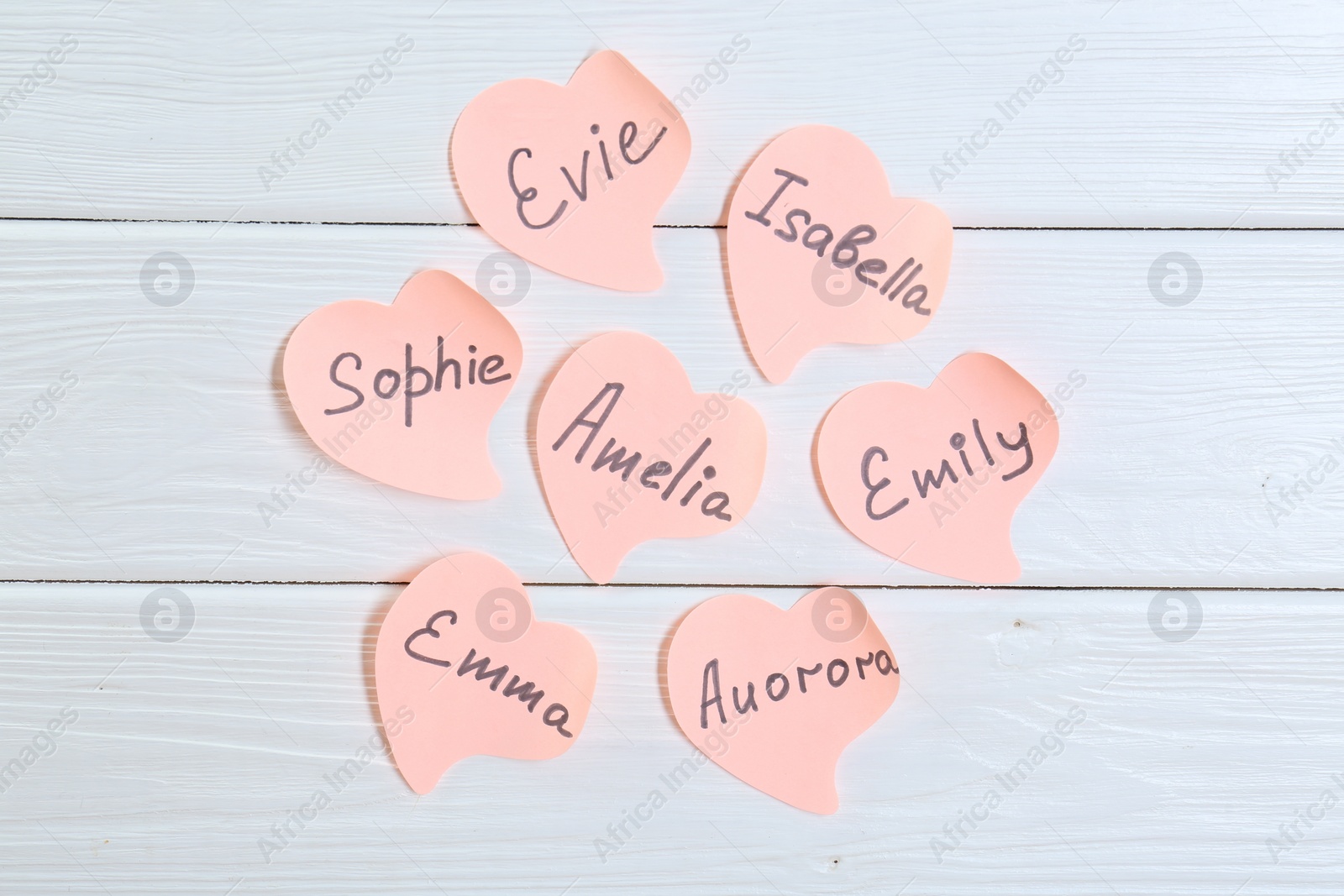 Photo of Paper stickers with different names on white wooden background, flat lay. Choosing baby's name