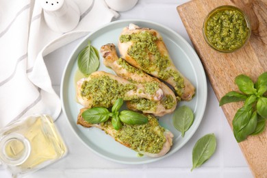 Delicious fried chicken drumsticks with pesto sauce and ingredients on white table, flat lay