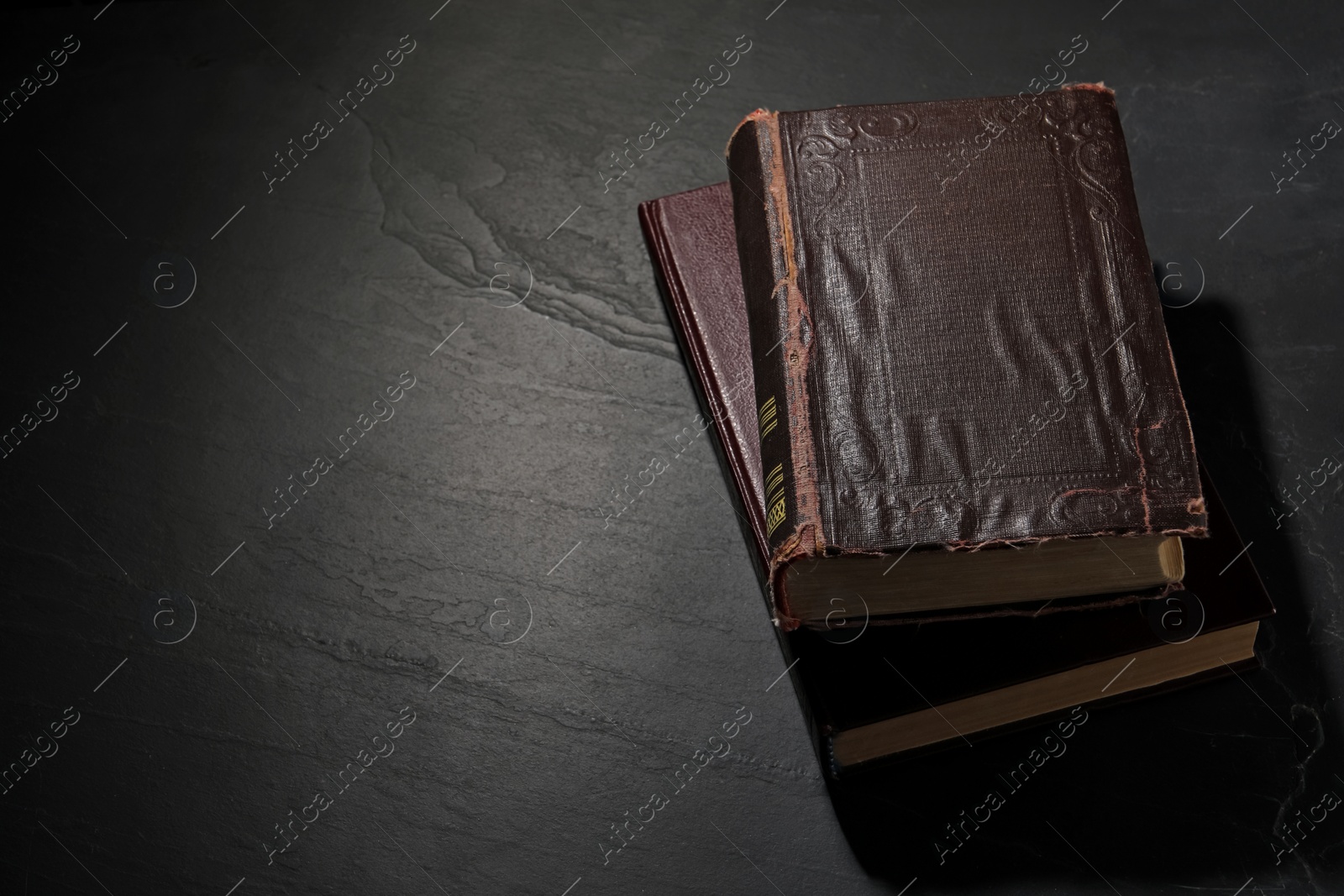 Photo of Old hardcover books on black textured table, space for text