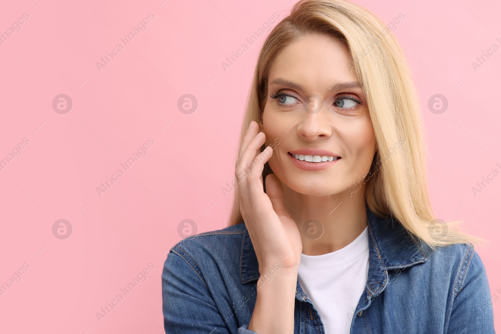 Photo of Portrait of smiling middle aged woman with blonde hair on pink background. Space for text