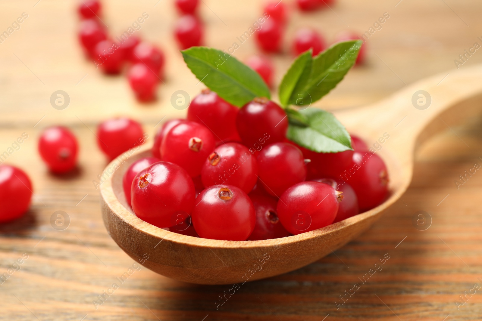 Photo of Spoon with tasty cranberries and green leaves on wooden table, closeup