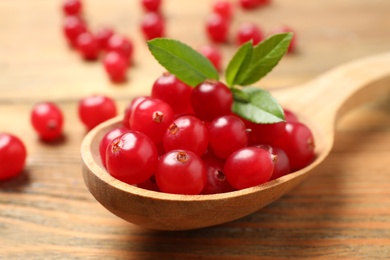 Spoon with tasty cranberries and green leaves on wooden table, closeup