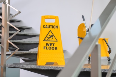 Safety sign with phrase Caution wet floor and mop bucket on stairs. Cleaning service