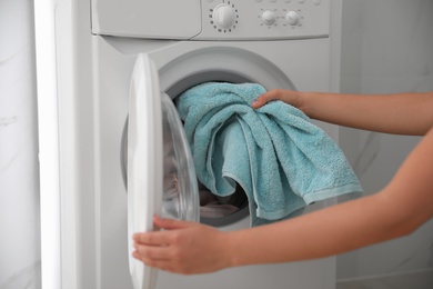 Woman putting dirty laundry into washing machine indoors, closeup