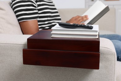 Photo of Remote control and books on sofa armrest wooden table. Man reading at home, closeup