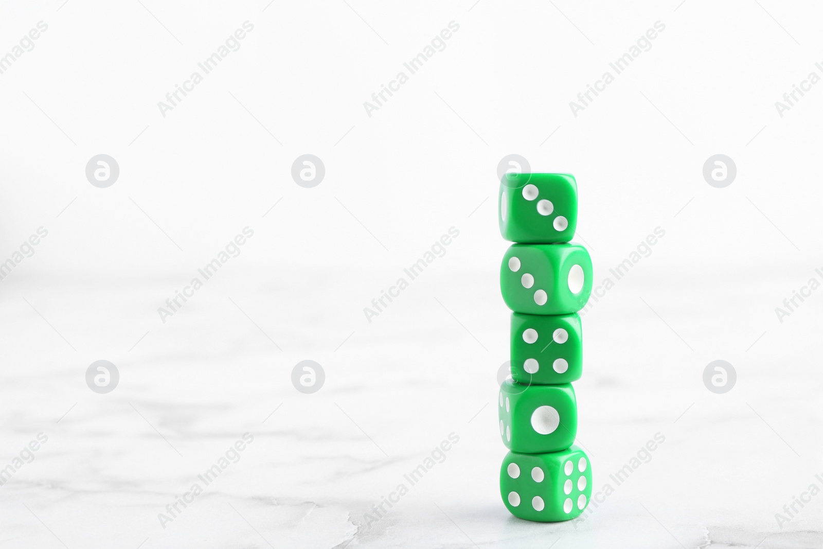 Photo of Many stacked green dices on white marble table. Space for text