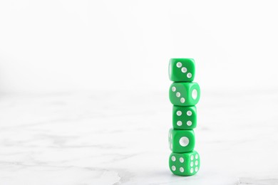 Many stacked green dices on white marble table. Space for text