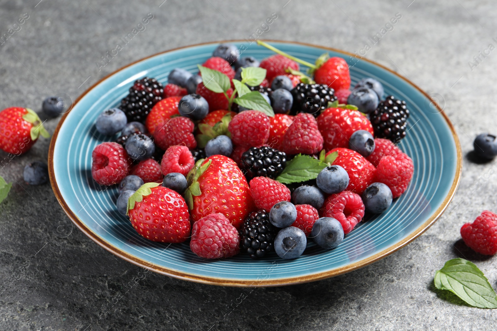 Photo of Many different fresh ripe berries in plate on grey table