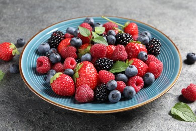 Photo of Many different fresh ripe berries in plate on grey table