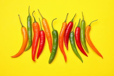Photo of Different hot chili peppers on yellow background, flat lay