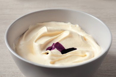Photo of Bowl of cream with purple food coloring on white wooden table, closeup