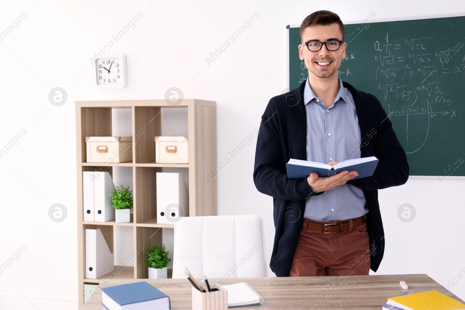 Photo of Young male teacher with book standing in classroom