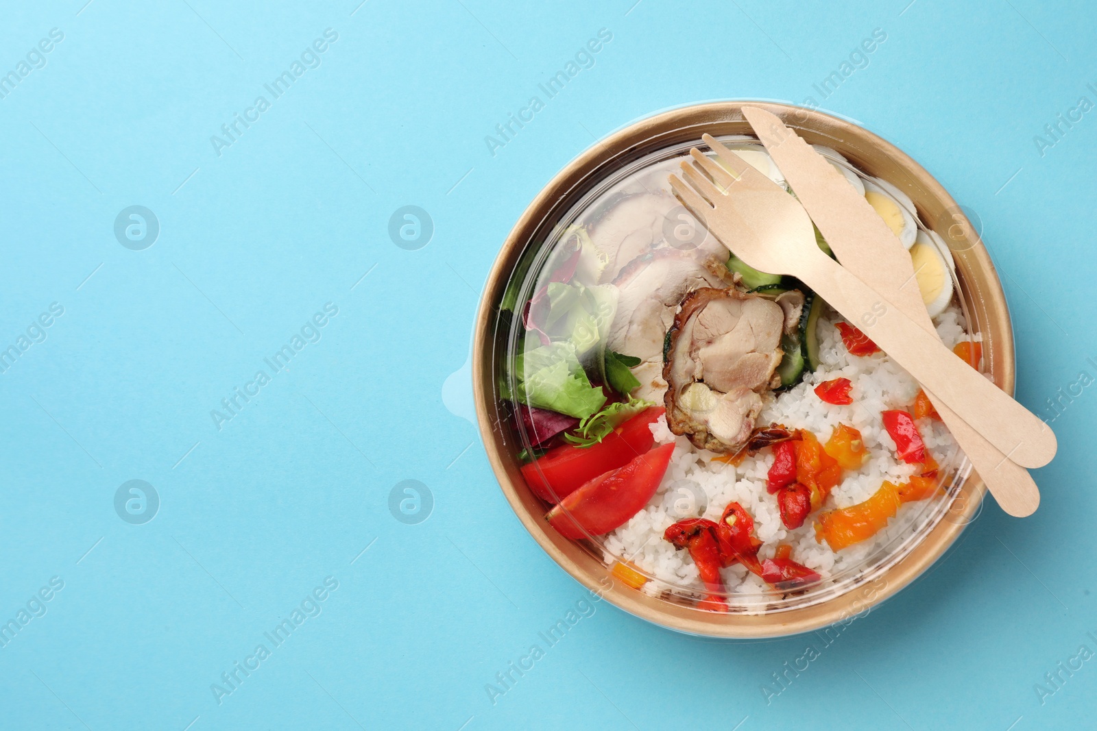 Photo of Tasty food in container with fork and knife on light blue background, top view. Space for text