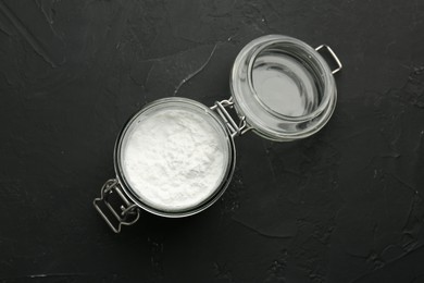 Baking powder in jar on black textured table, top view