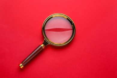 Magnifying glass on red background, top view