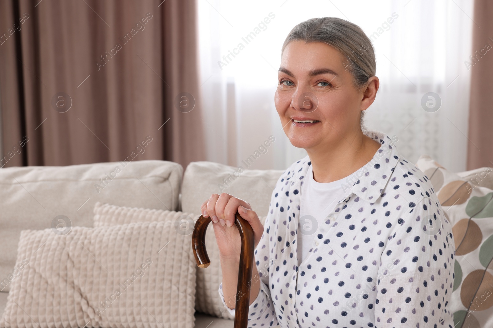 Photo of Senior woman with walking cane sitting on sofa at home. Space for text