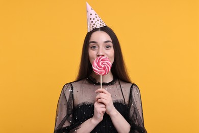 Woman in party hat holding lollipop on orange background