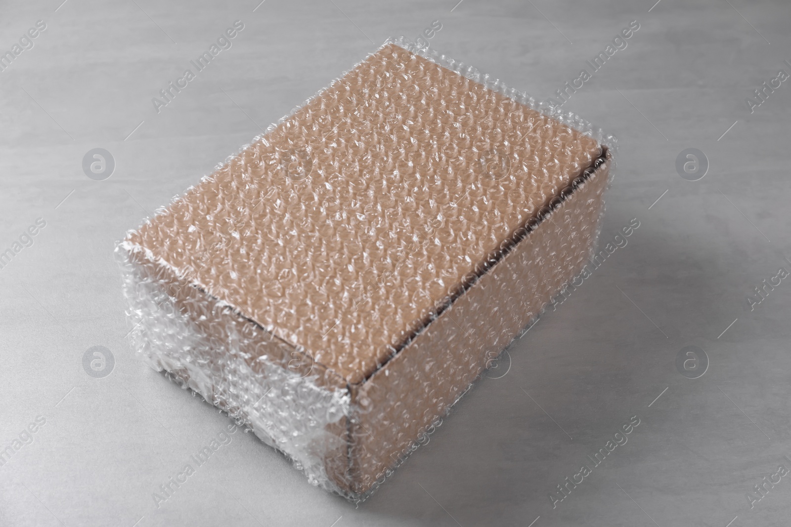 Photo of Cardboard box covered with bubble wrap on light grey table