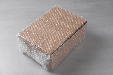 Photo of Cardboard box covered with bubble wrap on light grey table