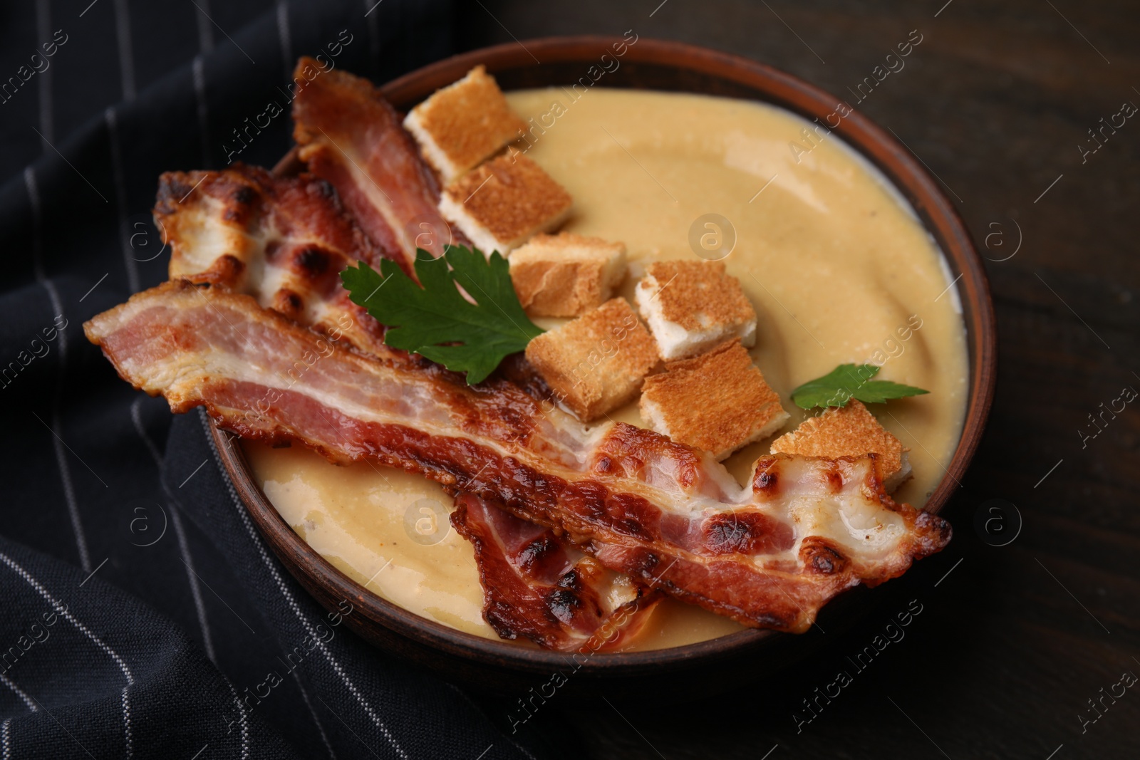 Photo of Delicious lentil soup with bacon and parsley in bowl on table, closeup