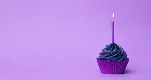 Photo of Delicious birthday cupcake with dark blue cream and burning candle on violet background. Space for text