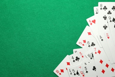 Photo of Scattered playing cards on green table, top view. Space for text