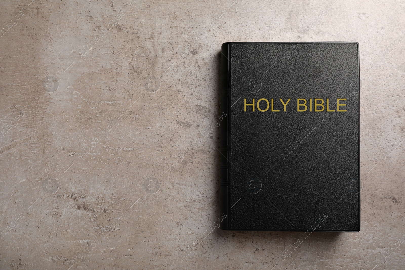 Photo of Bible with black cover on light grey table, top view. Space for text