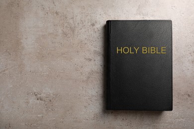 Photo of Bible with black cover on light grey table, top view. Space for text