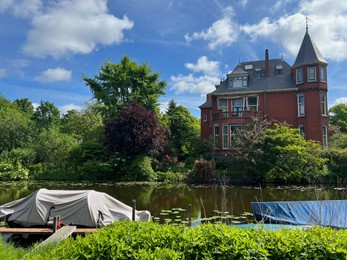 Beautiful view of house near river with moored boats on sunny day