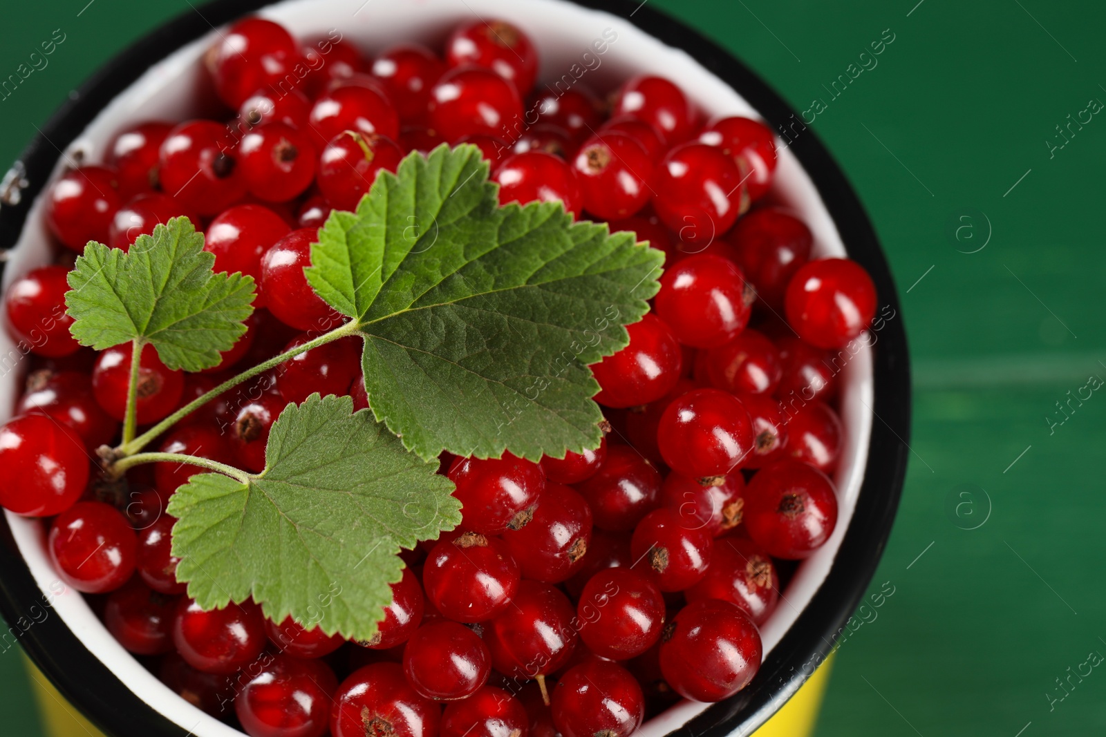 Photo of Ripe red currants and leaves in mug on green table, closeup